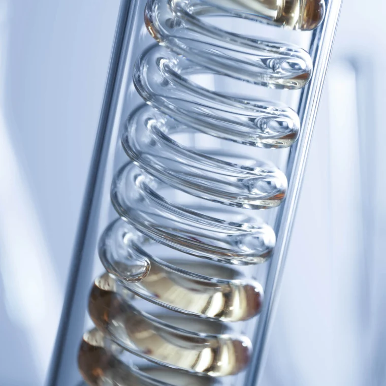 Close-up of a glass laboratory condenser coil, typically used in scientific and chemical experiments, with light reflecting off the surface.