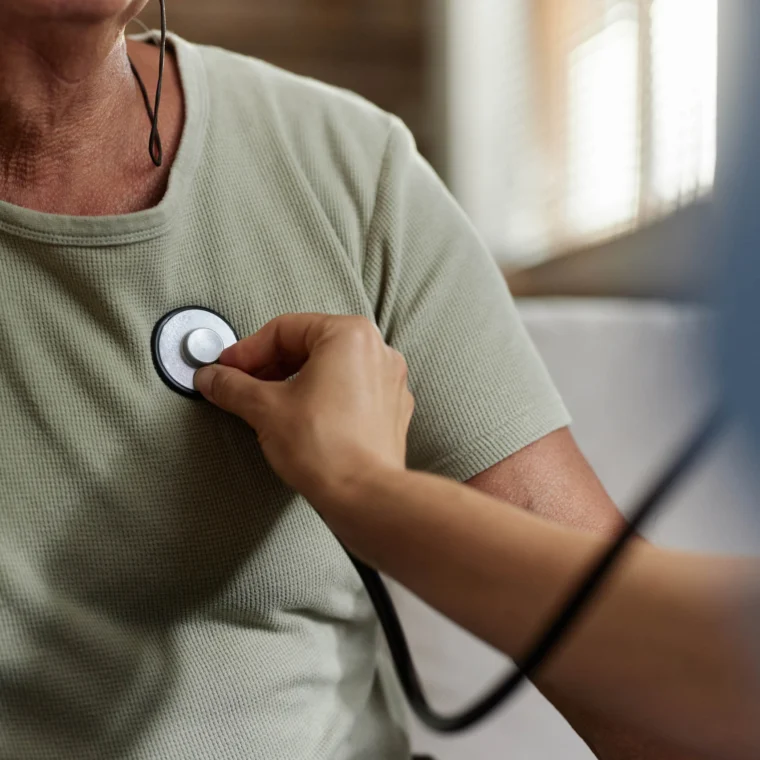 A healthcare worker uses a stethoscope to listen to the chest of a person wearing a green shirt.