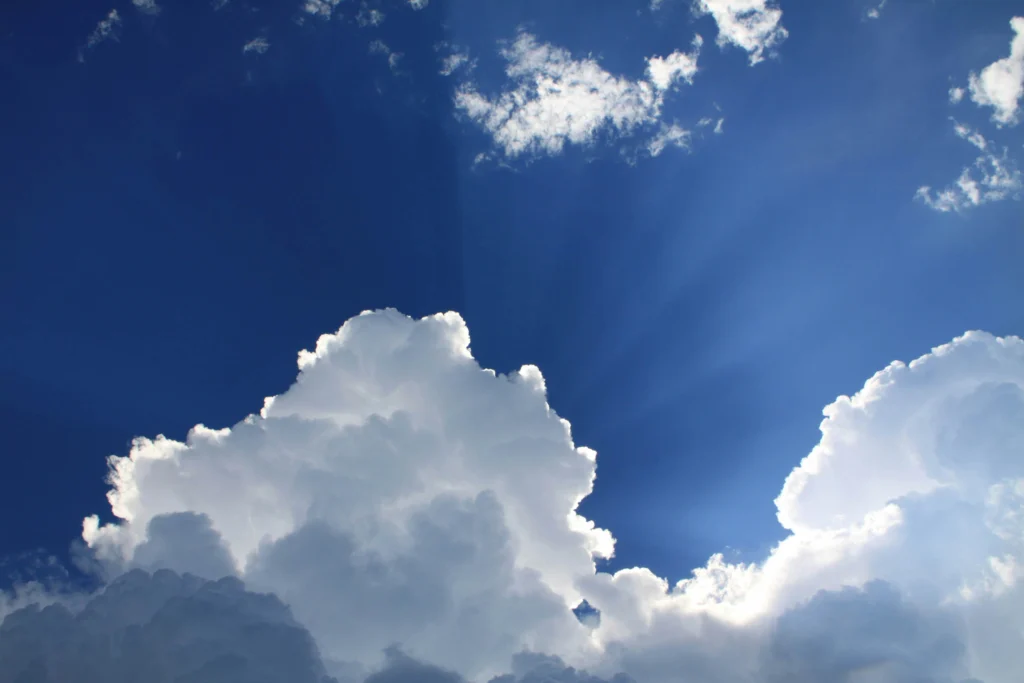 Large white clouds with sunlight streaming through against a deep blue sky.