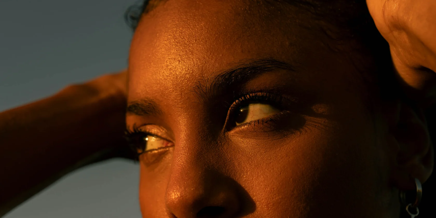 Close-up of a person's face with warm sunlight casting shadows, showing detailed skin texture and focus on their eyes looking to the side.
